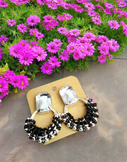 Pair of earrings with black beads and clear stones on a yellow card, placed on a floral fabric background.