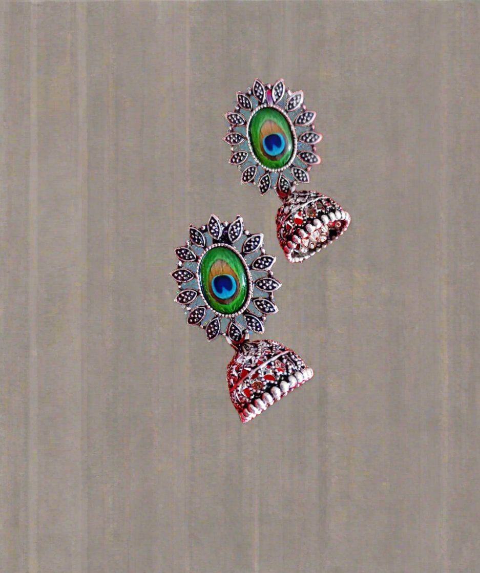 Decorative earrings with peacock feather design on a red fabric background